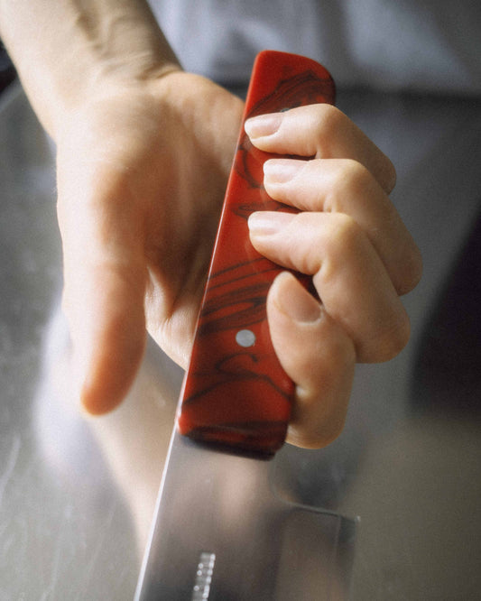 Hand holding a bistro santoku knife with a red handle